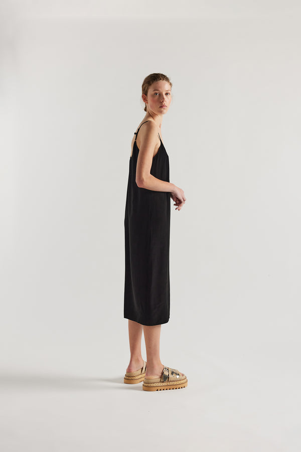 Side view of model in black Mid-length slip dress with straight neckline and relaxed silhouette