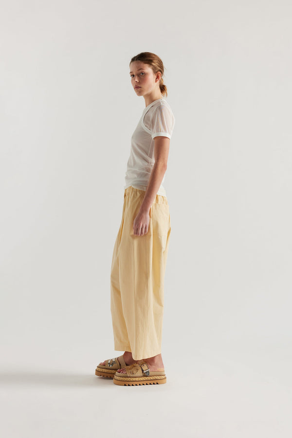 Side view of the model in the Factor Pleat Pant Buttermilk yellow. A relaxed silhouette defined by an encased elastic waistband. 
