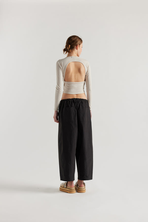 Back view of the model in the Factor Pleat Pant black slate. A relaxed silhouette defined by an encased elastic waistband. 