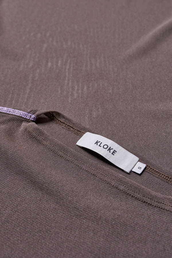 Close up details of the Flow Mesh Short Sleeve Top in Brown and Lilac. Featuring a high neckline, contrast flatlock seams, and sheer, lightweight fabric, perfect for layering. 