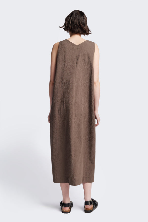 The back of the Long-length Forces Pinafore Dress in brown Kloke designed soft seersucker premium cotton . Relaxed fit with a deep rounded neckline, front patch pockets, and a front split for ease of movement. Available in 5 sizes. 