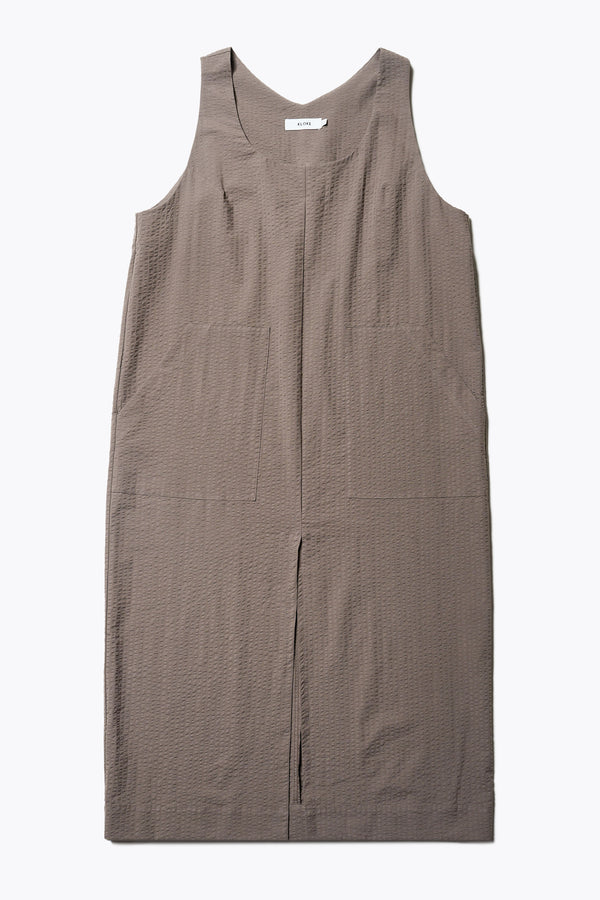 Long-length Forces Pinafore Dress in brown Kloke designed soft seersucker premium cotton. Relaxed fit with a deep rounded neckline, front patch pockets, and a front split for ease of movement. Available in 5 sizes. 