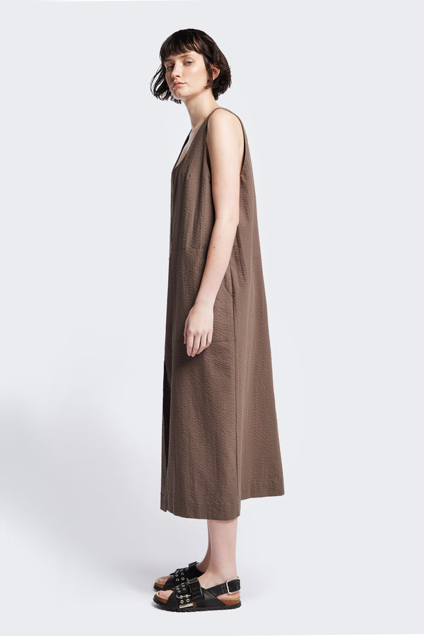 Side of Long-length Forces Pinafore Dress in brown Kloke designed soft seersucker premium cotton . Relaxed fit with a deep rounded neckline, front patch pockets, and a front split for ease of movement. Available in 5 sizes. 