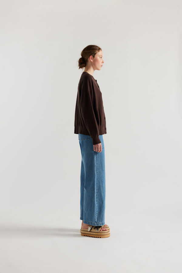 Side view of model in the brown cotton ribbed sweater with button closure and dropped shoulders.
