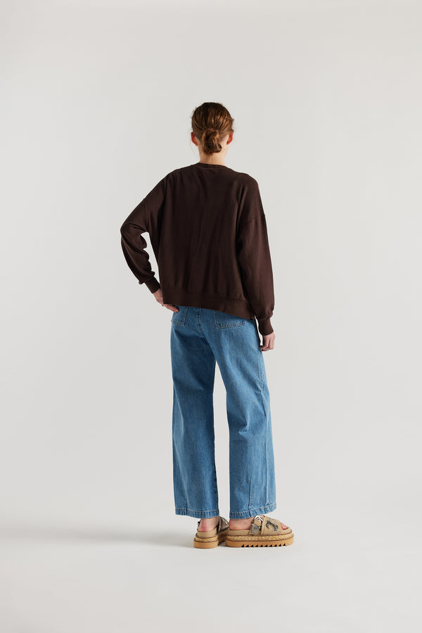 Back view of model in the brown cotton ribbed sweater with button closure and dropped shoulders.