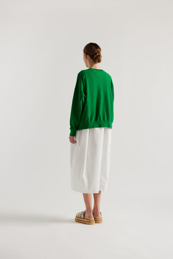 Back view of model in the green cotton ribbed sweater with button closure and dropped shoulders.