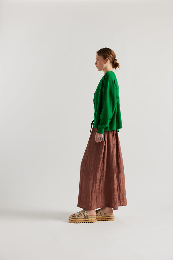 Side view of model in the green cotton ribbed sweater with button closure and dropped shoulders.