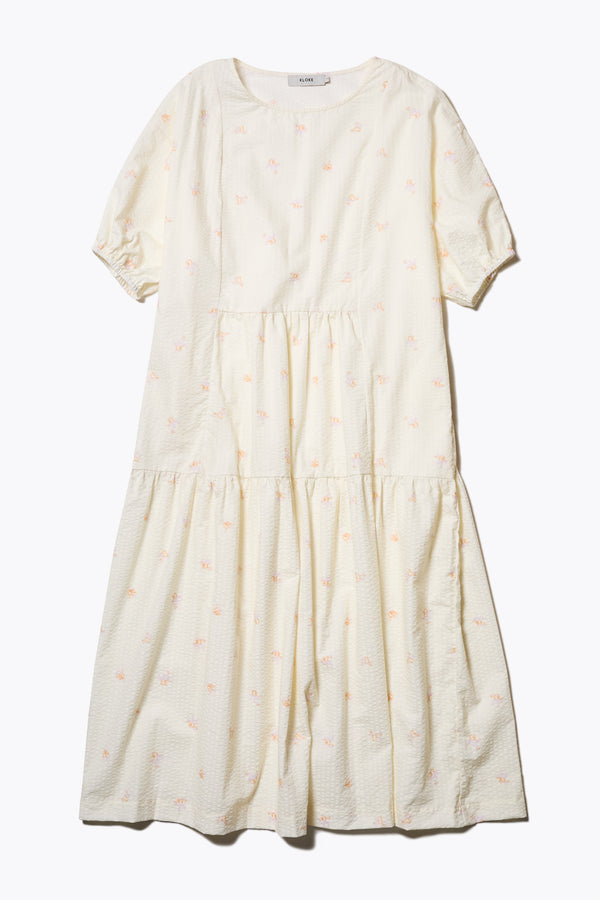 Flat Front of the Gradient Dress in Ecru, a panelled dropped sleeve dress in Kloke's floral seersucker print, featuring a tiered gathered skirt, in-seam pockets, and elastic cuff sleeves.  