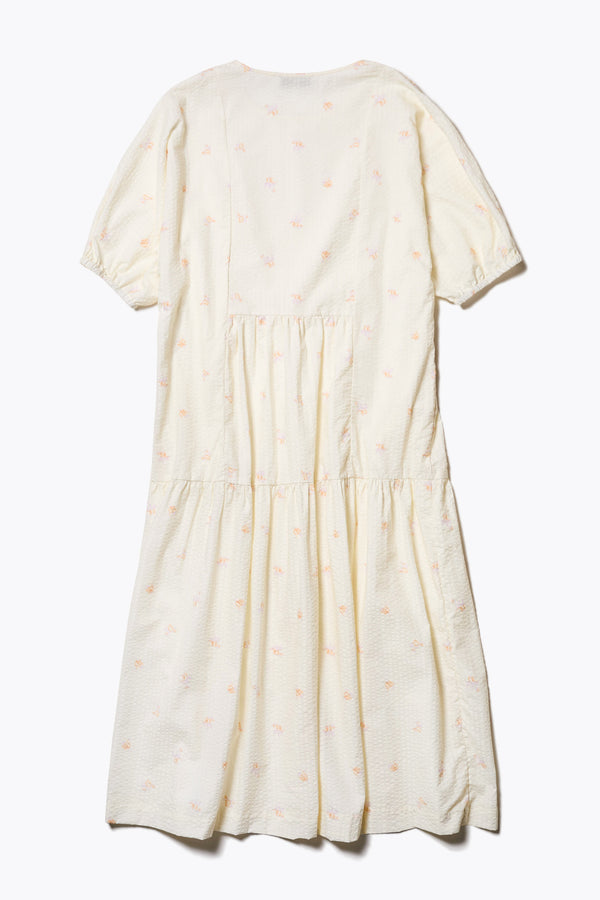 Flat Back of the Gradient Dress in Ecru, a panelled dropped sleeve dress in Kloke's floral seersucker print, featuring a tiered gathered skirt, in-seam pockets, and elastic cuff sleeves.  