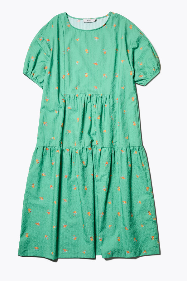 Flat Front of the Gradient Dress in Green, a panelled dropped sleeve dress in Kloke's floral seersucker print, featuring a tiered gathered skirt, in-seam pockets, and elastic cuff sleeves.  