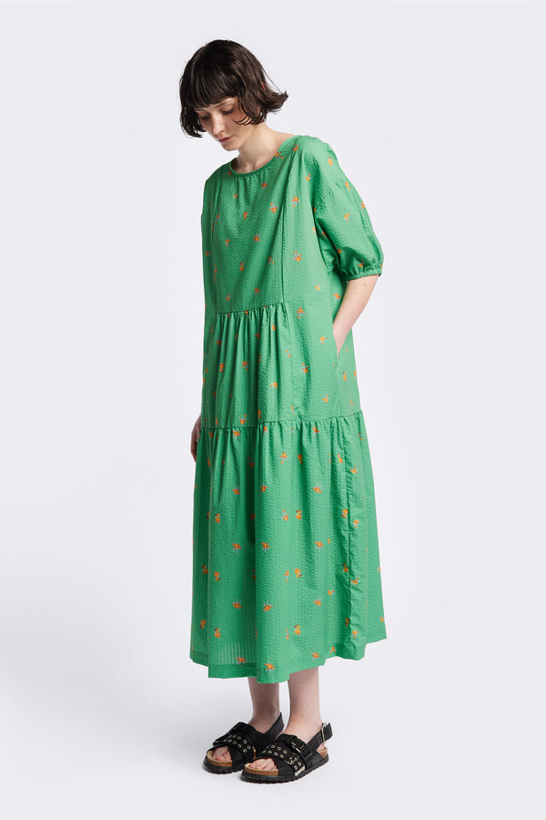 Front of the Gradient Dress in Green, a panelled dropped sleeve dress in Kloke's floral seersucker print, featuring a tiered gathered skirt, in-seam pockets, and elastic cuff sleeves.  