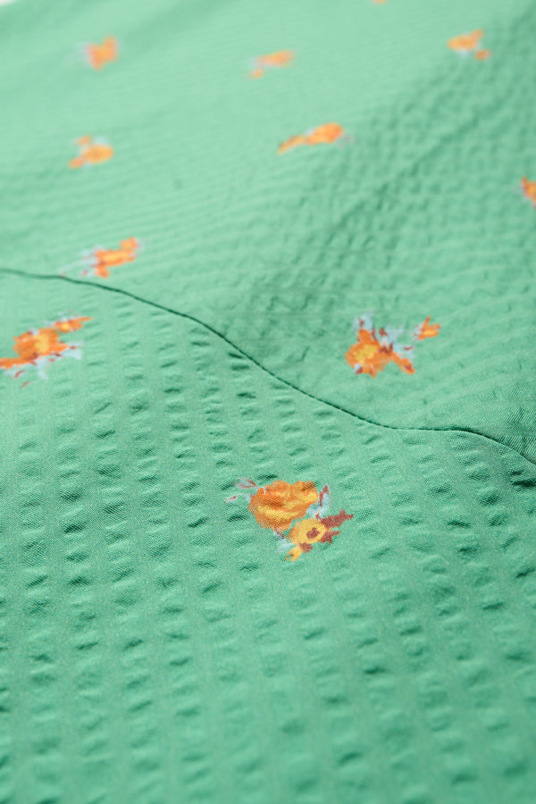 Fabric close up of the Gradient Dress in Green, a panelled dropped sleeve dress in Kloke's floral seersucker print, featuring a tiered gathered skirt, in-seam pockets, and elastic cuff sleeves.  