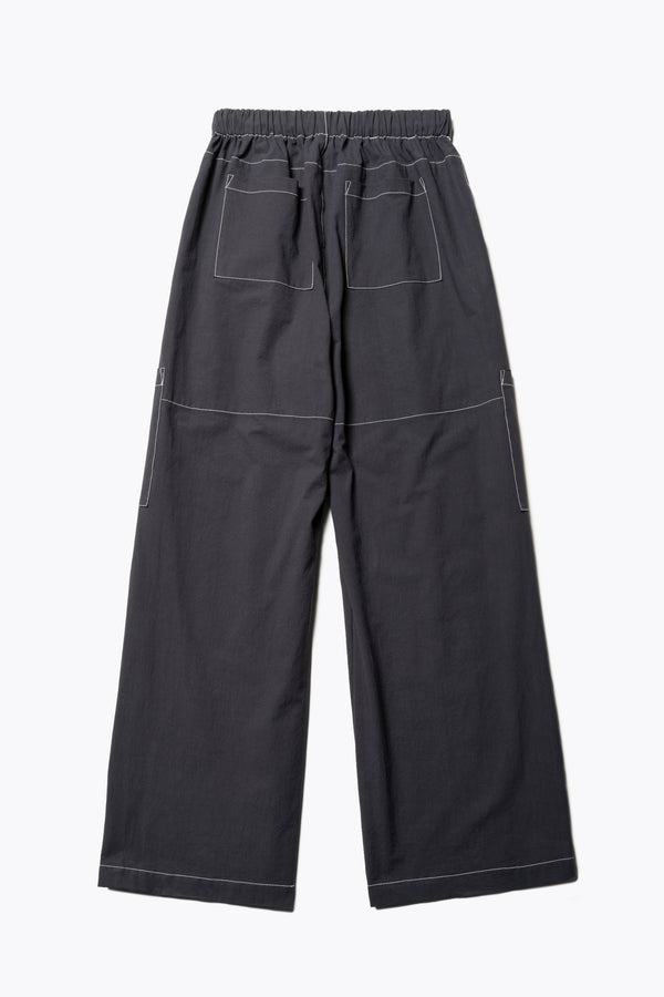 Flat back of the black Helius Beach Pant in lightweight fabric with contrast stitching, pocket detailing, and an adjustable elastic waistband with a tie pull.