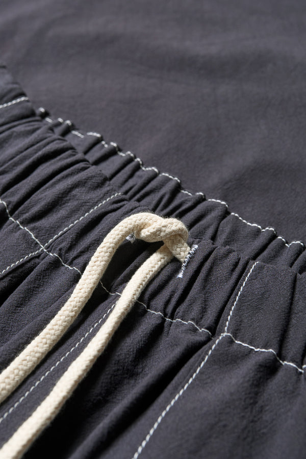 Close up details of the black Helius Beach Pant in lightweight fabric with contrast stitching, pocket detailing, and an adjustable elastic waistband with a tie pull.