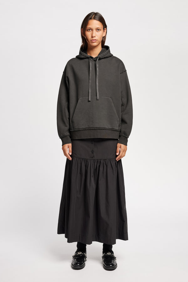 Front of Model wearing relaxed-fit fleece hoodie in black with raw seams and blind-stitched finishing, inspired by classic sportswear silhouettes.