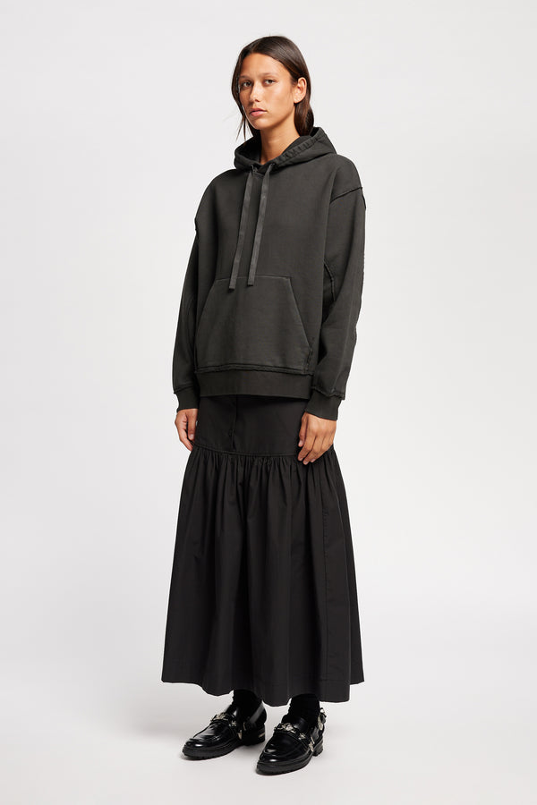 Front of Model wearing relaxed-fit fleece hoodie in black with raw seams and blind-stitched finishing, inspired by classic sportswear silhouettes.
