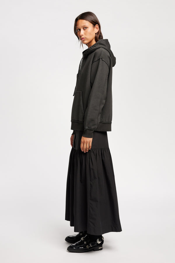 Side of Model wearing relaxed-fit fleece hoodie in black with raw seams and blind-stitched finishing, inspired by classic sportswear silhouettes.