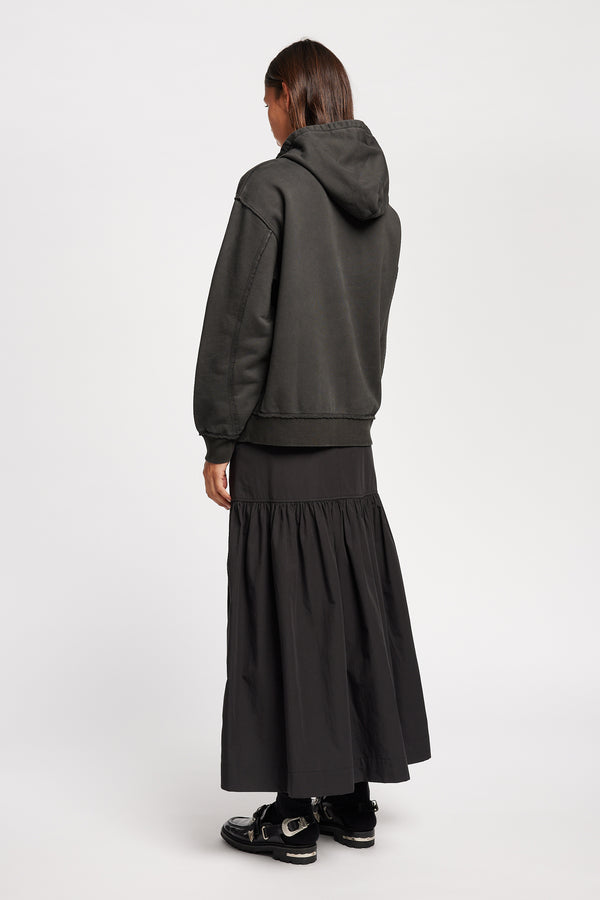 Back of Model wearing relaxed-fit fleece hoodie in black with raw seams and blind-stitched finishing, inspired by classic sportswear silhouettes.