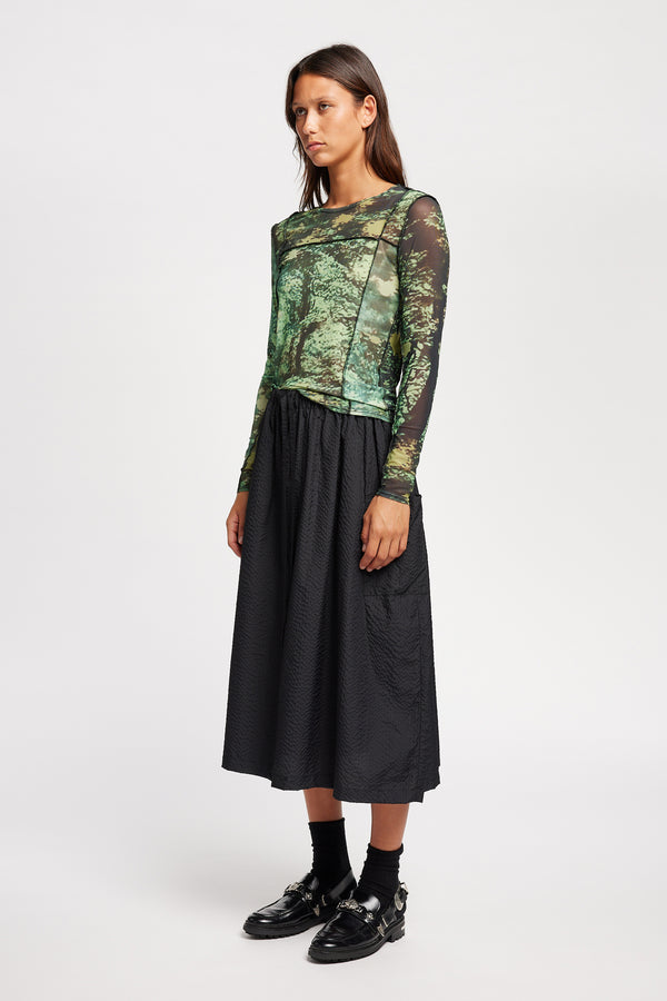 Front view of model in the Inlet Top in Real Tree green print, featuring a slim fit, semi-sheer mesh fabric, and black baby lock stitching.