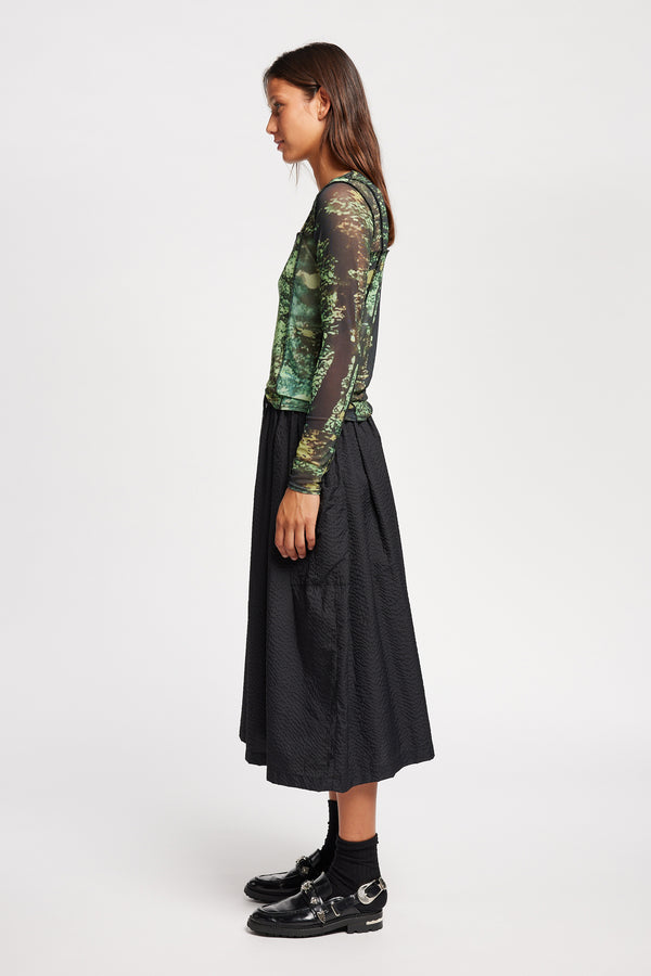 Side view of model in the Inlet Top in Real Tree green print, featuring a slim fit, semi-sheer mesh fabric, and black baby lock stitching.