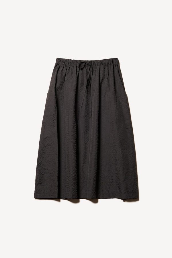 Flat front of the Jet black Minor Skirt, an A-line midi skirt with an elastic waistband and soft gathered detailing, in lightweight Japanese seersucker.