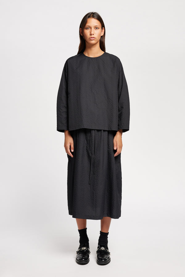 Front view of model wearing the Jet black Minor Skirt, an A-line midi skirt with an elastic waistband and soft gathered detailing, in lightweight Japanese seersucker.