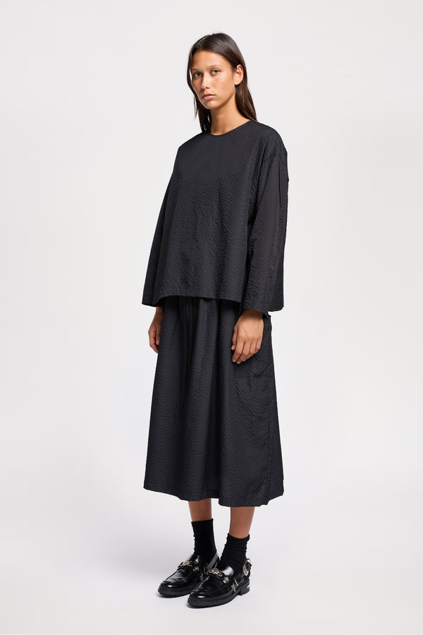 Front view of model wearing the Jet black Minor Skirt, an A-line midi skirt with an elastic waistband and soft gathered detailing, in lightweight Japanese seersucker.