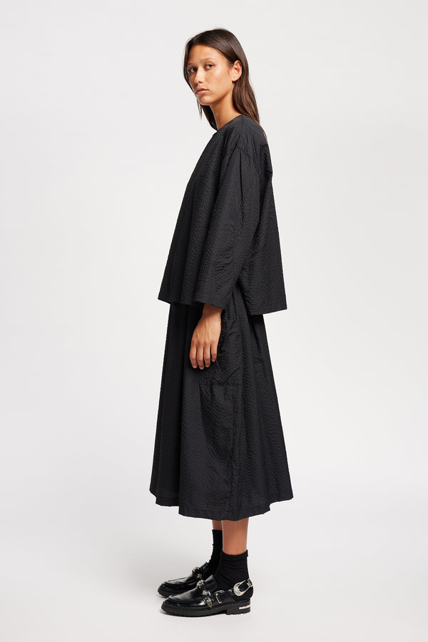 Side view of model wearing the Jet black Minor Skirt, an A-line midi skirt with an elastic waistband and soft gathered detailing, in lightweight Japanese seersucker.