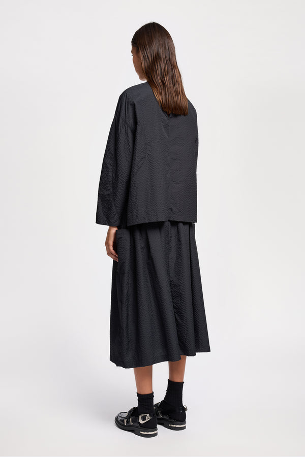 Back view of model wearing the Jet black Minor Skirt, an A-line midi skirt with an elastic waistband and soft gathered detailing, in lightweight Japanese seersucker.