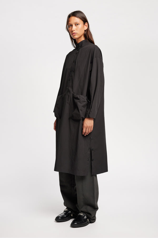 Front of Model wearing the Odeum Dress in black mid-weight cotton, featuring a high mock collar and large utility pockets.
