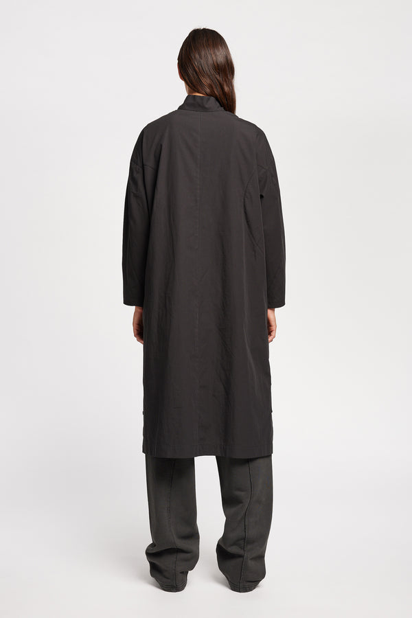 Back of Model wearing the Odeum Dress in black mid-weight cotton, featuring a high mock collar and large utility pockets.