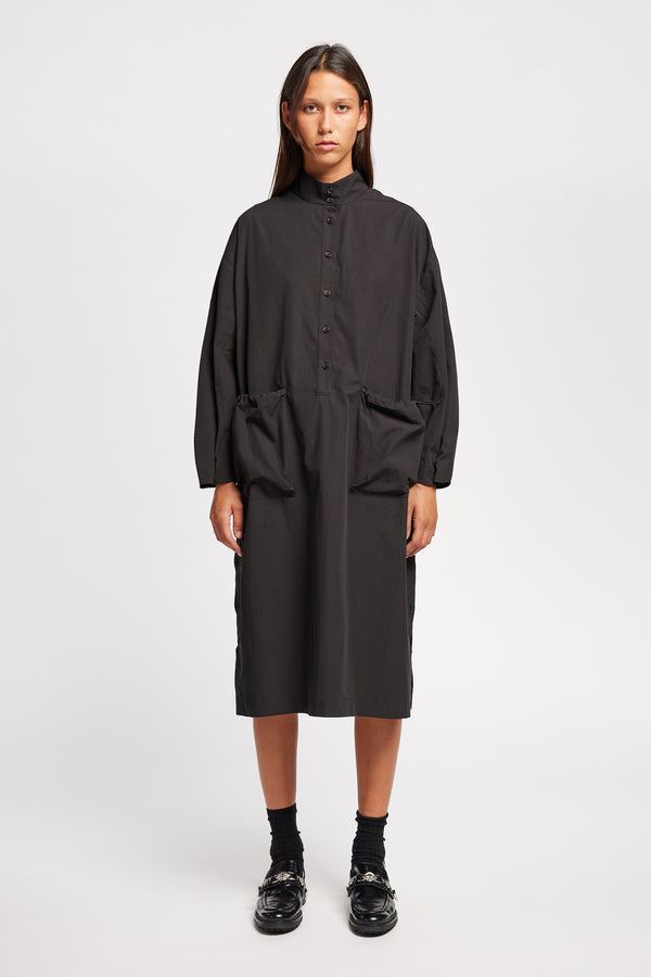 Front of Model wearing the Odeum Dress in black mid-weight cotton, featuring a high mock collar and large utility pockets.