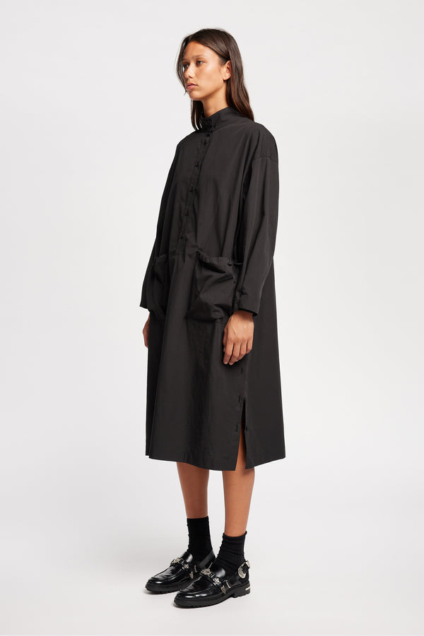 Front of Model wearing the Odeum Dress in black mid-weight cotton, featuring a high mock collar and large utility pockets.