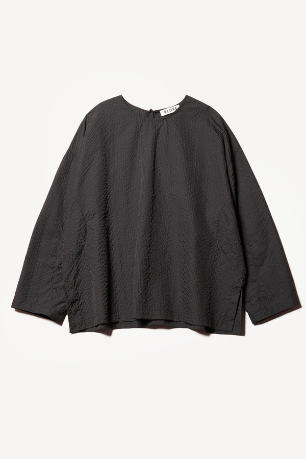 Flat Front of the Omit Top, a relaxed-fit Japanese seersucker top in Jet Black with dropped sleeves and a round neckline.