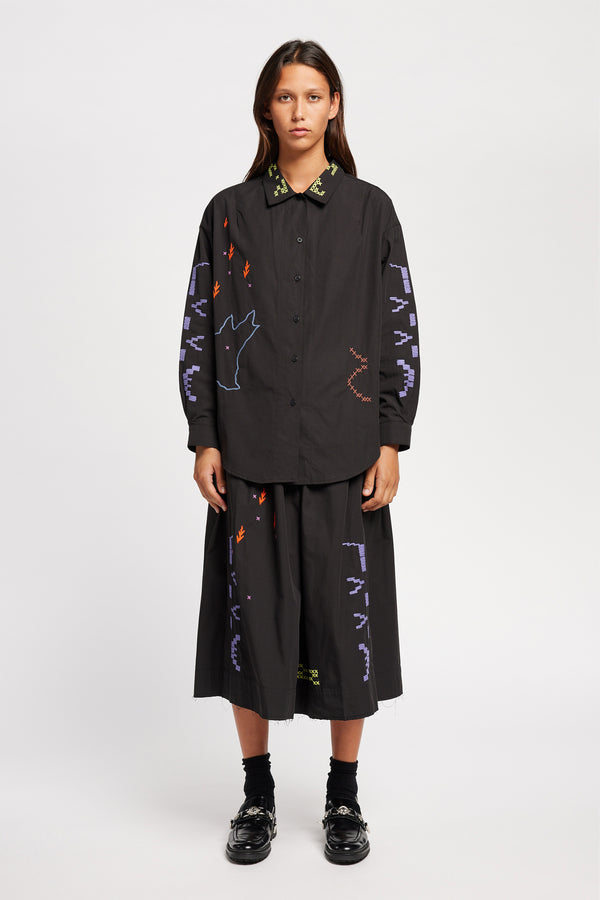 Front of model wearing Black One World shirt with embroidered Arecibo motifs on collar, sleeves, and front. Classic collar and full placket.