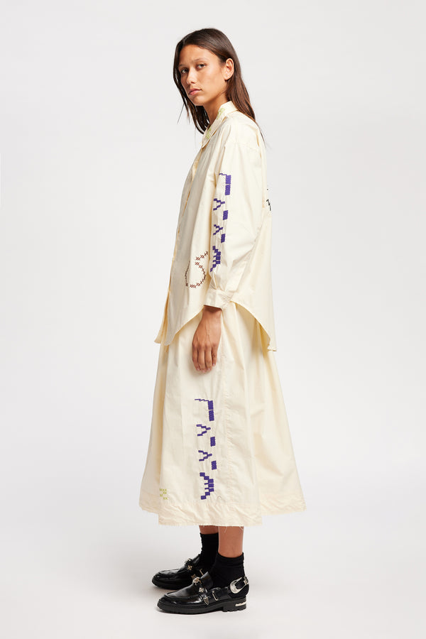 Side of model wearing Ecru button-up shirt with embroidered Arecibo motifs on collar, sleeves, and front. Classic collar and full placket.