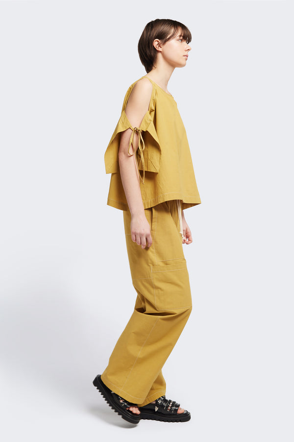 Side view of the Open Shoulder Top in mustard. Featuring a relaxed fit and side-tie sleeve details.