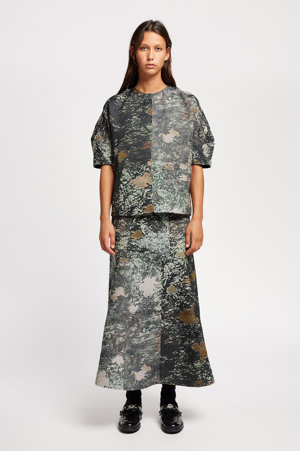 Front view model in the Optic Skirt a midi-length A-line skirt in textured jacquard green print fabric with a forest-inspired pattern, designed by Kloke