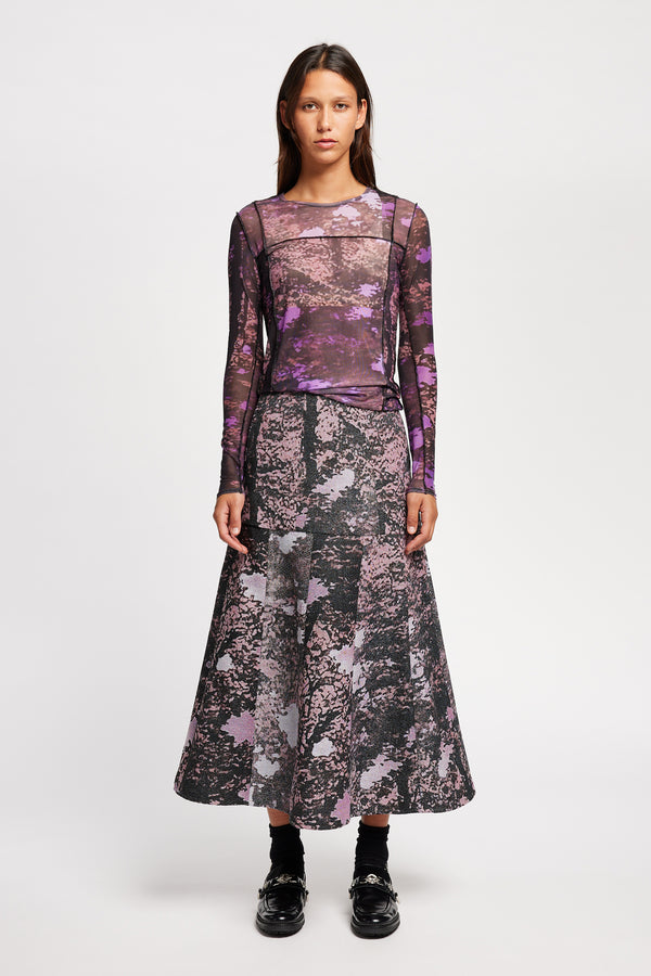 Front view model in the Optic Skirt a midi-length A-line skirt in textured jacquard purple print fabric with a forest-inspired pattern, designed by Kloke