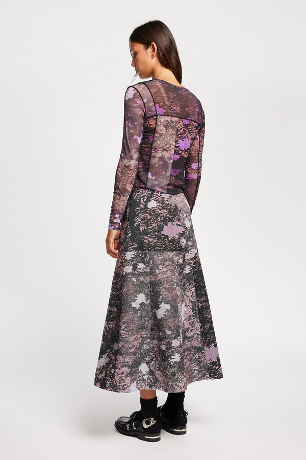Back view model in the Optic Skirt a midi-length A-line skirt in textured jacquard purple print fabric with a forest-inspired pattern, designed by Kloke