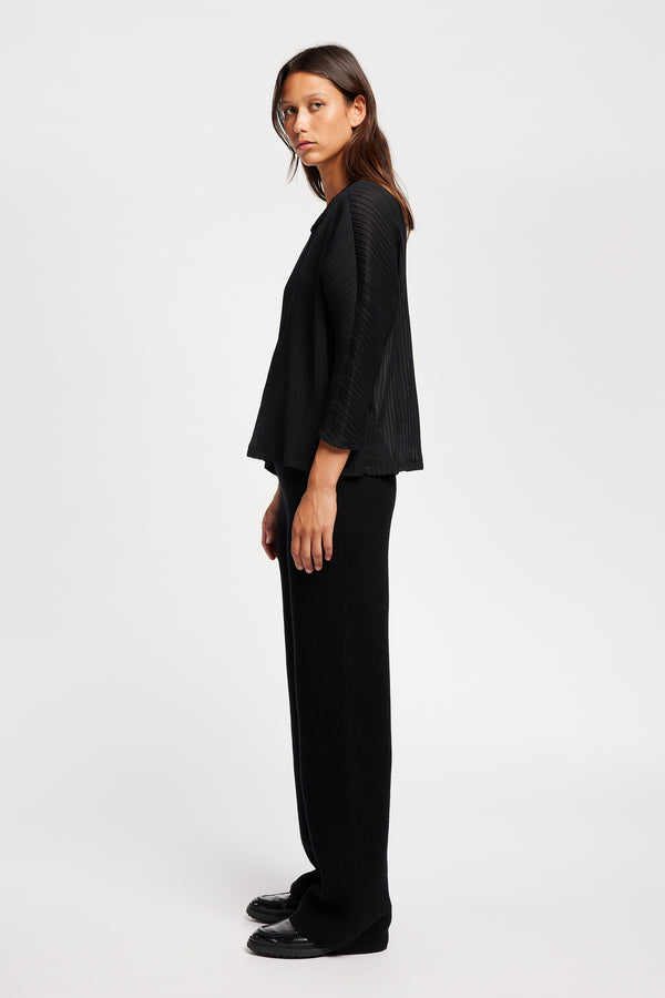 Side of Model wearing the Loose-fit crinkle top in black made from Japanese recycled polyester, featuring panelled seams and a textured finish.
