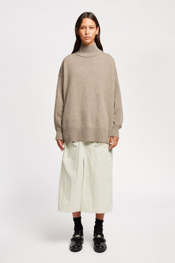 Front view of Model wearing Overflow long knit, high neck wool blend sweater with exposed seams in taupe