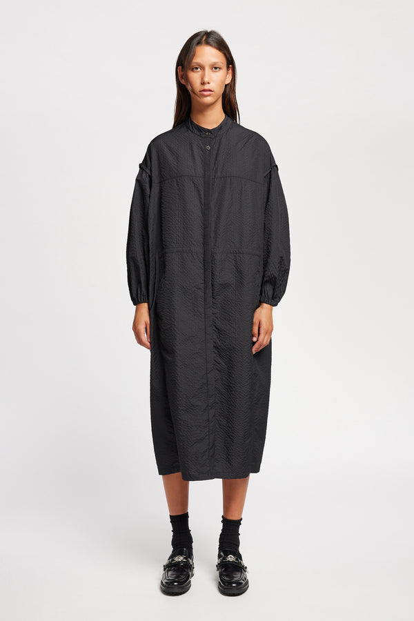 Front of Model wearing the Parapet Dress in Jet Black. A lightweight seersucker nylon, showing band collar and adjustable front waist tie.