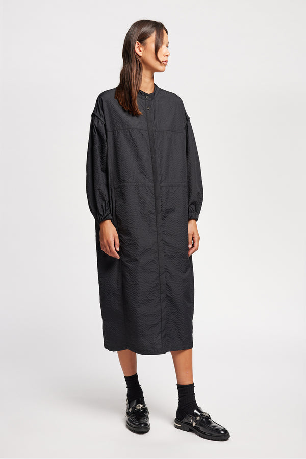 Front of Model wearing the Parapet Dress in Jet Black. A lightweight seersucker nylon, showing band collar and adjustable front waist tie.