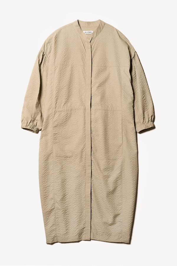 Flat front of the Parapet Dress in Stone/beige. A lightweight seersucker nylon, showing band collar and adjustable front waist tie.