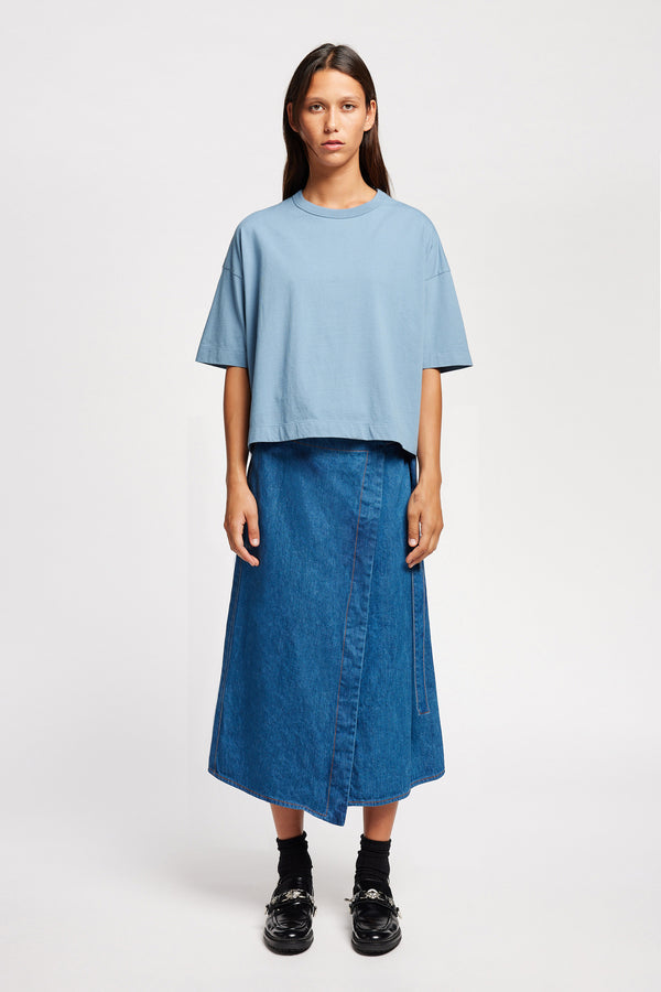 Front view of model wearing  Parity wrap denim skirt in mid blue with A-line silhouette. made from 100% Japanese Denim. 

