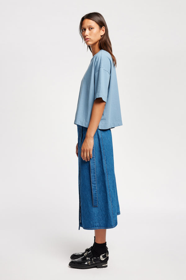Side view of model wearing  Parity wrap denim skirt in mid blue with A-line silhouette. made from 100% Japanese Denim. 
