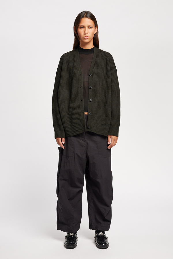 Front view of model wearing oversized ribbed wool cardigan with button closure in Darkest Green