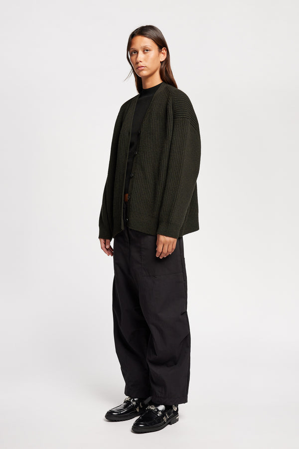 Front angle view of model wearing oversized ribbed wool cardigan with button closure in darkest green