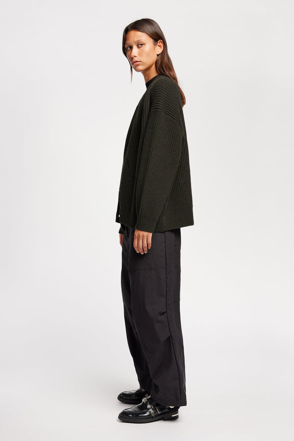 Side view of model wearing oversized ribbed wool cardigan with button closure in darkest green